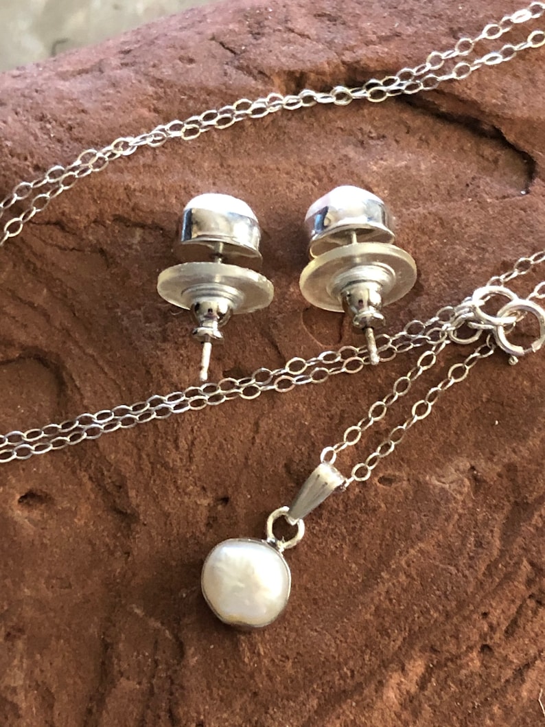 May include: A silver necklace with a pearl pendant and matching pearl stud earrings. The necklace has a delicate chain and the pearl pendant is round and white.