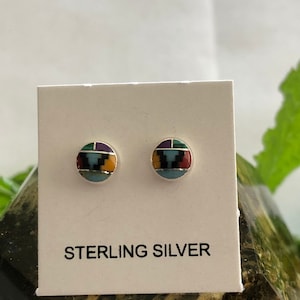 May include: Two round sterling silver stud earrings with colorful inlaid designs. Each earring features a mosaic pattern with turquoise, black, yellow, and red accents. The earrings are displayed on a white card with the text "STERLING SILVER".