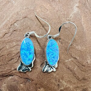 May include: A pair of silver dangle earrings with blue opal stones. The earrings have a floral design.