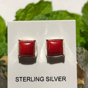 May include: A pair of sterling silver earrings with square red coral stones. The earrings are displayed on a white card with the text "STERLING SILVER".