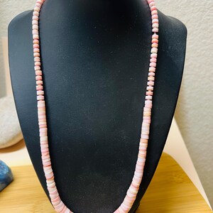 May include: A long necklace made of pink and white shell beads. The beads are round and have a smooth, polished finish.