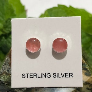 May include: A pair of sterling silver stud earrings with pink gemstone accents. The earrings are displayed on a white card with the text "STERLING SILVER".