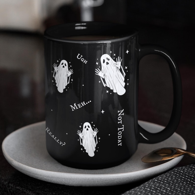 May include: A black ceramic mug featuring three white ghost illustrations and the text "Ugh," "Meh...", "Not Today," and "Really?" printed in white. The mug has a curved handle and is decorated with small white star accents scattered around the ghosts.