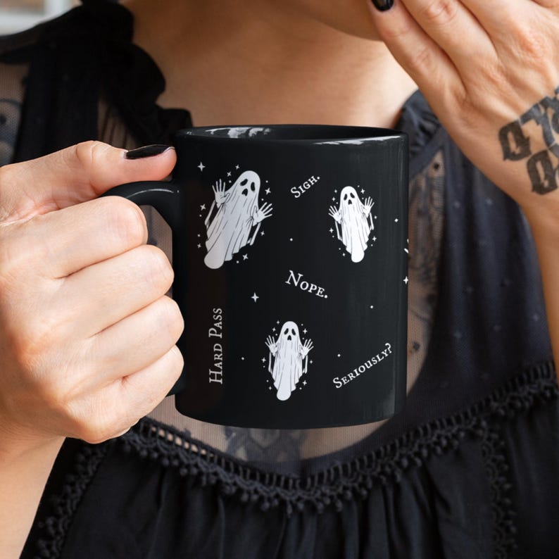 May include: A black ceramic mug featuring a repeating pattern of white ghost illustrations and the text "Sigh.", "Nope.", "Hard Pass", and "Seriously?" interspersed with small white star icons across the exterior surface of the drinkware.