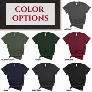 May include: A collection of seven short-sleeved crew neck t-shirts displayed in various solid colors including asphalt, military green, forest, maroon, navy, dark gray, and black. Each shirt is tied at the side and labeled with its color name.