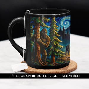 May include: A black ceramic mug featuring a colorful, stained-glass style illustration of a Bigfoot creature hiding behind a tree in a forest, with a hiker in the distance and a swirling night sky. A tea bag string hangs over the rim of the mug.