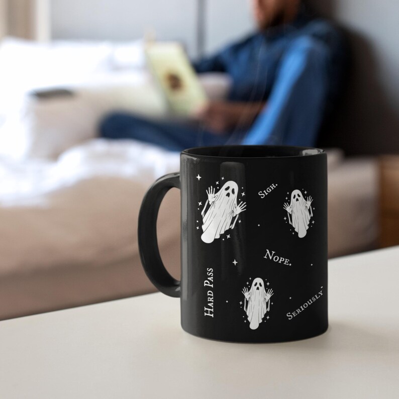 May include: A black ceramic mug featuring three white ghost illustrations with raised hands, surrounded by small star icons. The text printed on the mug includes the words SIGH, NOPE, HARD PASS, and SERIOUSLY, arranged around the ghost graphics.