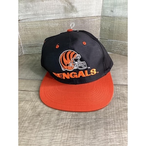 May include: Black and orange Bengals baseball cap. The cap features the team's helmet logo in orange and white, with the word "Bengals" in orange. The brim is orange, and the crown is black.