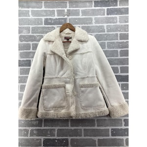 May include: A cream-colored jacket featuring a soft, fuzzy faux-shearling collar, cuffs, and hem trim. The jacket has a button-front closure, two large front patch pockets with fuzzy trim, and visible seam detailing across the chest and waist.