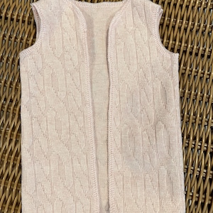 K&ouml;nnte beinhalten: Eine hellrosa Weste ohne &Auml;rmel mit einem strukturierten Strickmuster in Rautenform. Das &auml;rmellose Kleidungsst&uuml;ck hat einen runden Halsausschnitt und einen geraden Saum. Die Weste ist aus einem weichen, leichten Material gefertigt.
