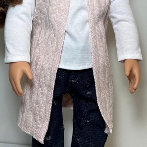 K&ouml;nnte beinhalten: Eine Puppe tr&auml;gt einen hellrosa Cardigan mit offener Vorderseite &uuml;ber einem wei&szlig;en Langarmshirt und einer dunkelblauen Jeans mit Used-Look. Der Cardigan hat ein strukturiertes Muster.