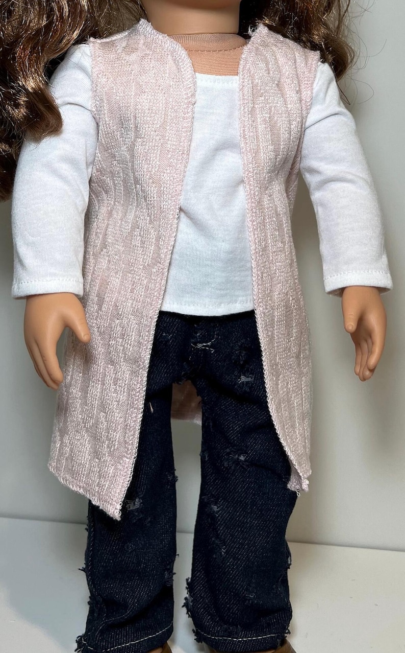 K&ouml;nnte beinhalten: Eine Puppe tr&auml;gt einen hellrosa Cardigan mit offener Vorderseite &uuml;ber einem wei&szlig;en Langarmshirt und einer dunkelblauen Jeans mit Used-Look. Der Cardigan hat ein strukturiertes Muster.