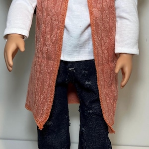 K&ouml;nnte beinhalten: Eine Puppe tr&auml;gt ein wei&szlig;es Langarmshirt, eine dunkelblaue Jeans mit Used-Look und eine strukturierte orangefarbene Weste. Die Puppe tr&auml;gt auch braune Schuhe. Das Outfit ist f&uuml;r eine Puppe entworfen.