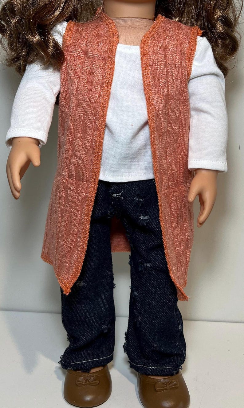 K&ouml;nnte beinhalten: Eine Puppe tr&auml;gt ein wei&szlig;es Langarmshirt, eine dunkelblaue Jeans mit Used-Look und eine strukturierte orangefarbene Weste. Die Puppe tr&auml;gt auch braune Schuhe. Das Outfit ist f&uuml;r eine Puppe entworfen.