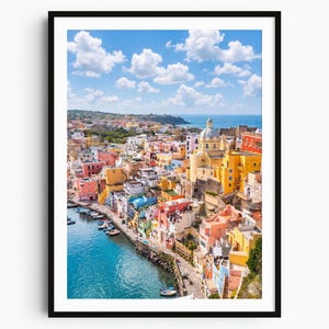 May include: A framed vertical wall art print featuring a high-angle view of a coastal Italian town with colorful buildings in shades of yellow, pink, and orange, a large domed church, a blue harbor with small boats, and a bright blue sky with clouds.