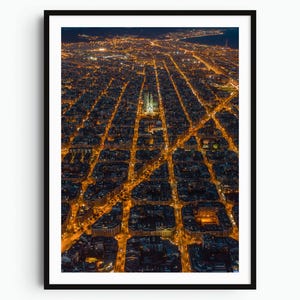 May include: An aerial night view of a city grid featuring a large, illuminated cathedral at the center. The urban landscape is characterized by a dense pattern of square city blocks outlined by bright orange streetlights against the dark night.