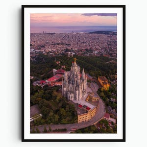 May include: An aerial view of the Temple of the Sacred Heart of Jesus in Barcelona, featuring a stone church with a golden statue atop a hill, surrounded by dense green trees, with the sprawling city and a pink sunset sky in the background.