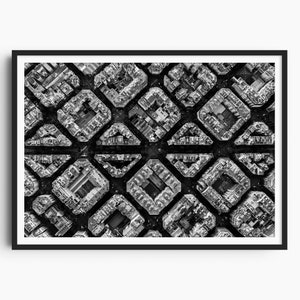 May include: A black and white aerial photograph of a city, showing a geometric pattern of buildings. The buildings are arranged in a grid pattern, creating a sense of order and symmetry.