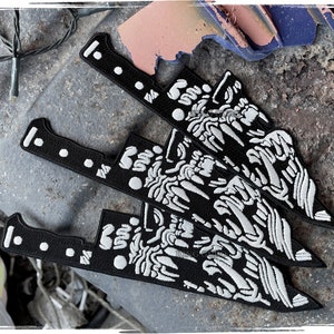 May include: Three black embroidered patches shaped like knives with white detailed designs. The patches have a white stitched handle and a white stitched blade with a detailed design.