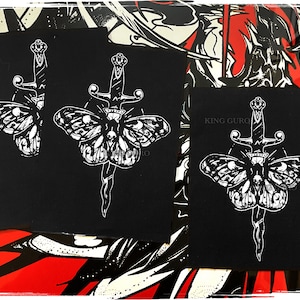 May include: Three black fabric patches with white embroidered designs of a butterfly with a dagger through it. The text "KING GURO" is visible on one patch.