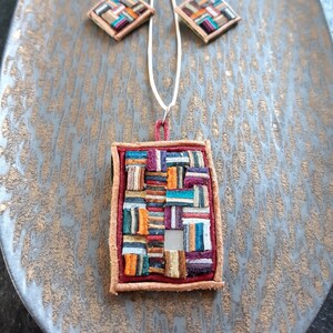 May include: A colorful necklace and earrings set with a rectangular pendant and diamond-shaped earrings. The pendant and earrings are made of a patchwork of colorful leather pieces.