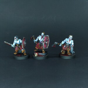 May include: Three painted miniature figures of undead warriors with axes and shields. The figures are posed in a fighting stance and are painted in shades of white, red, and black.