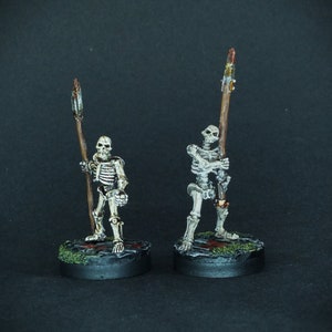 May include: Two painted skeletal figures holding spears, standing on black bases with green and brown accents. The figures are posed in a fighting stance.