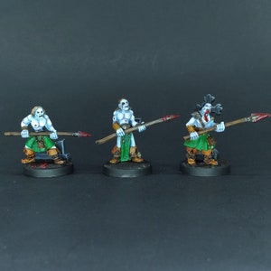 May include: Three painted miniature figures of warriors holding spears. The figures are painted in shades of blue, green, and brown. The figures are standing on black bases.