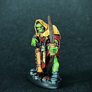 Peut inclure: Figurine miniature d'un archer orc à la peau verte. L'orc porte une cape à capuche jaune et une tunique rouge, tenant un arc et un carquois. La figurine est posée sur un socle texturé, peint avec des couleurs sombres. Pour jeux de table.