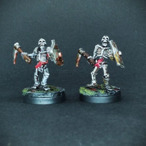 May include: Two painted skeletal figures holding weapons and shields. The figures are posed in a fighting stance and are standing on black bases with green and red accents.