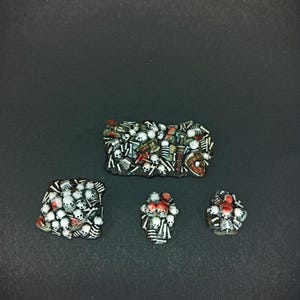 Puede incluir: Cuatro piezas de terreno en miniatura pintadas a mano para juegos de mesa. Las piezas representan montones de calaveras y huesos, con detalles en rojo. Las piezas están diseñadas para parecer un campo de batalla.