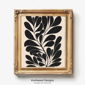 Op de afbeelding: Een ingelijste zwart-wit abstracte kunstprint van gestileerde bladeren op een cr&egrave;mekleurige achtergrond. De lijst is van licht hout.