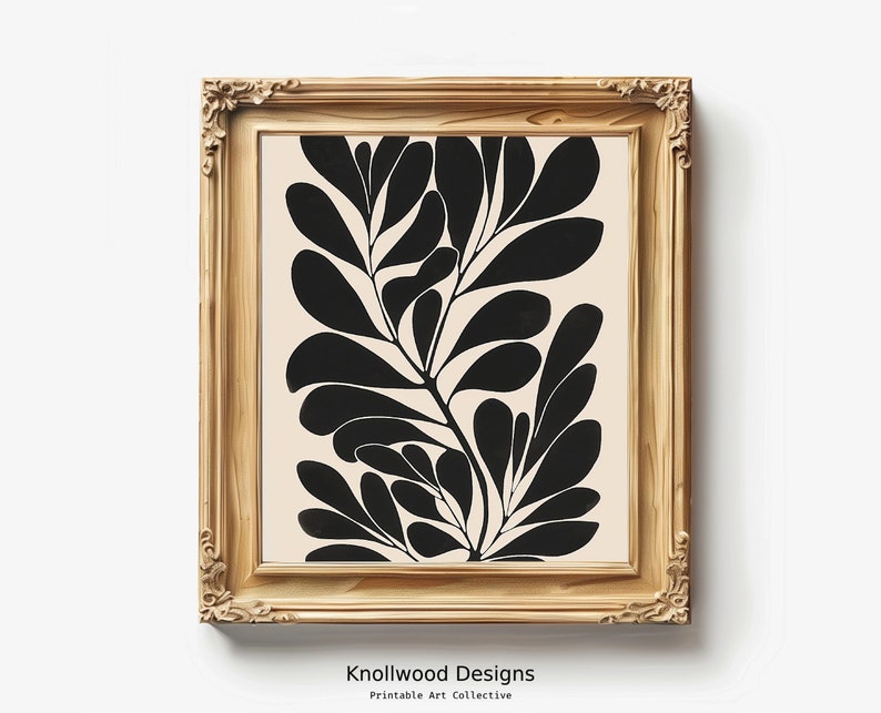 Op de afbeelding: Een ingelijste zwart-wit abstracte kunstprint van gestileerde bladeren op een cr&egrave;mekleurige achtergrond. De lijst is van licht hout.