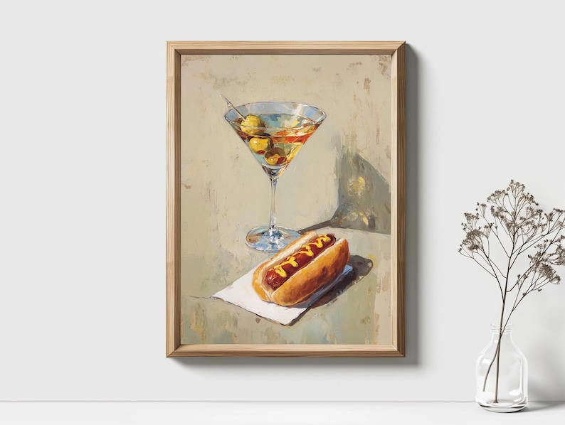May include: A framed painting depicts a martini with olives and a hot dog with mustard on a napkin. The painting has a light color palette with a wooden frame. The martini glass is tall and slender, and the hot dog is in a bun.