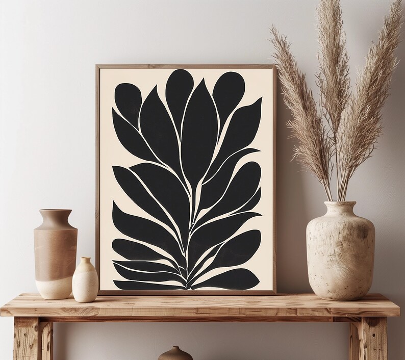 Op de afbeelding: Zwart-witte abstracte kunstprint van een gestileerde plant met grote bladeren. De print is ingelijst en wordt tentoongesteld op een houten plank met twee vazen.