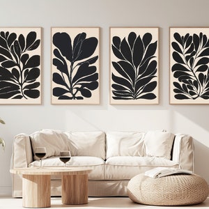 Op de afbeelding: Vier zwart-witte abstracte kunstprints van gestileerde bladeren, ingelijst in een licht houten lijst, hangen aan een witte muur boven een beige bank en een houten salontafel.