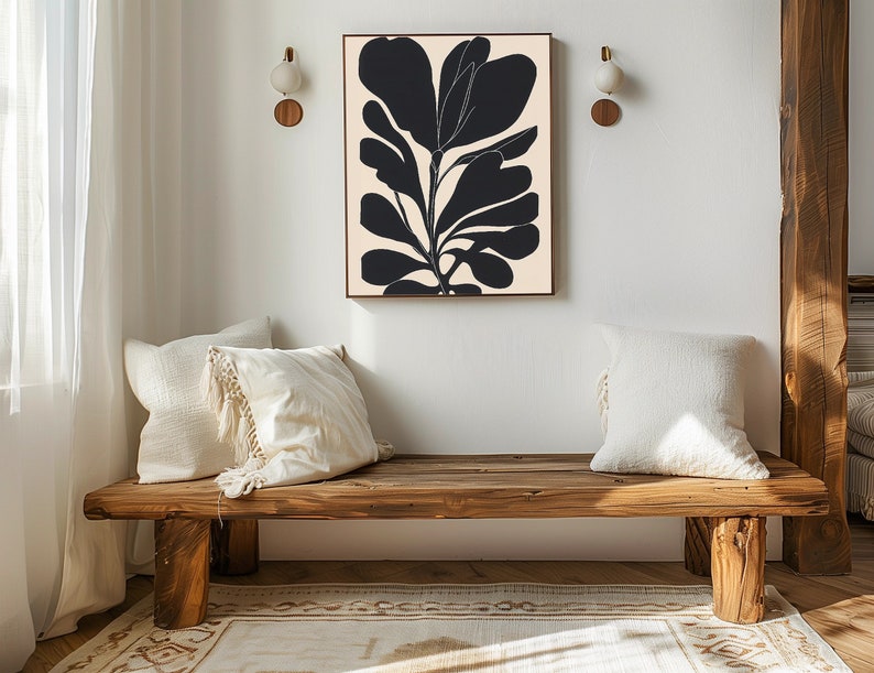 Op de afbeelding: Een houten bank met twee witte kussens staat voor een witte muur met een zwart-witte abstracte bloemenprint die eraan hangt.