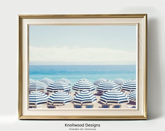 May include: A photograph of a beach scene with blue and white striped beach umbrellas lined up on the sand. The ocean is in the background.