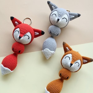 K&ouml;nnte beinhalten: Drei geh&auml;kelte Tier-Spielzeuge mit l&auml;chelnden Gesichtern. Die Spielzeuge sind ein roter Fuchs, ein grauer Fuchs und ein orangefarbener Fuchs. Jedes Spielzeug hat einen wei&szlig;en geh&auml;kelten Schwanz.