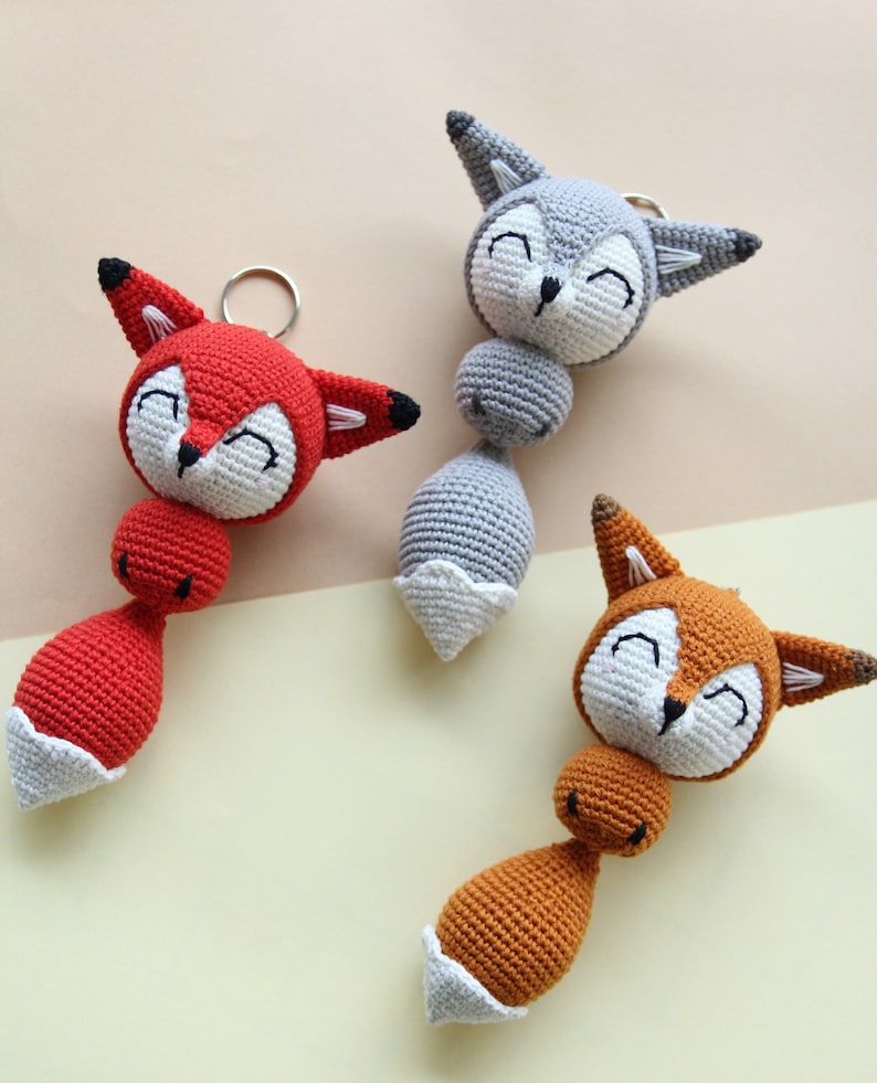 K&ouml;nnte beinhalten: Drei geh&auml;kelte Tier-Spielzeuge mit l&auml;chelnden Gesichtern. Die Spielzeuge sind ein roter Fuchs, ein grauer Fuchs und ein orangefarbener Fuchs. Jedes Spielzeug hat einen wei&szlig;en geh&auml;kelten Schwanz.