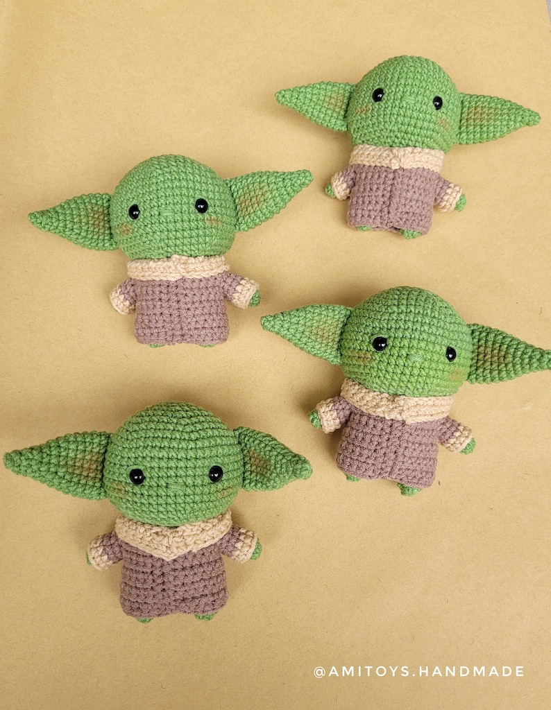 May include: Four crocheted green and brown plush toys shaped like a popular fictional character. The toys have large eyes and small ears. The toys are on a light brown surface. @AMITOYS.HANDMADE