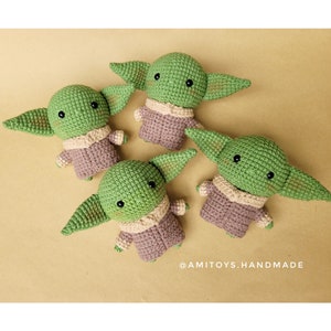 May include: Four crocheted green and brown plush toys shaped like a fictional character with large ears. The toys are sitting on a beige surface. The text '@amitoys.handmade' is visible in the bottom right corner of the image.