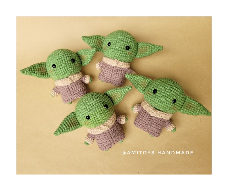 May include: Four crocheted green and brown plush toys shaped like a fictional character with large ears. The toys are sitting on a beige surface. The text '@amitoys.handmade' is visible in the bottom right corner of the image.