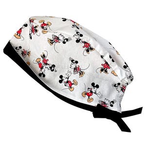 May include: White surgical scrub cap featuring a repeating pattern of Mickey Mouse in various poses. The cap has a black band and ties. The cartoon character is depicted in red, black, yellow, and white.