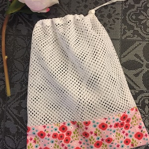 Peut inclure: Sac à linge en maille blanche avec une bordure florale rose et rouge. Le sac a une fermeture à cordon.