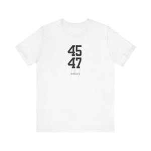 以下が含まれることがあります： 黒色の文字で「45 47」と書いてある白いTシャツ。下に小さな署名がある。