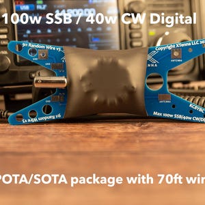 May include: A blue electronic component with the text "9:1 Random Wire v3" and "Copyright XTenna LLC 2025". The component is connected to a radio and includes the text "Max 100w SSB/40w CW/Digital". The image also includes the text "POTA/SOTA package with 70ft wire".
