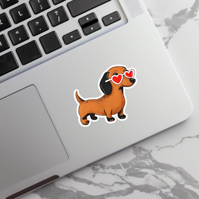 May include: A sticker featuring a cartoon dachshund wearing heart-shaped sunglasses. The dog is brown with black ears and paws. The sunglasses have red heart lenses and white frames. The sticker is placed on a laptop.