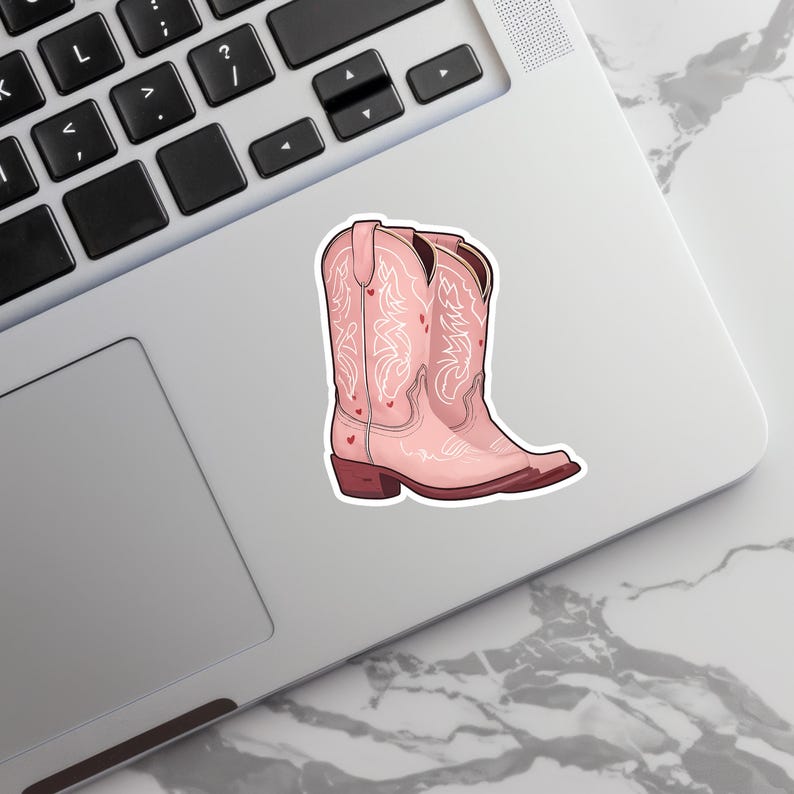 May include: A pink cowboy boot sticker with white decorative stitching and small red heart accents. The boot has a pointed toe and a brown heel. The sticker is placed on a laptop.