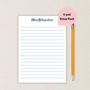 May include: A white notepad with blue horizontal lines and the name "Miss Richardson" in blue script. A pink label reads "6 pad Value Pack." A yellow pencil with a pink eraser rests beside the notepad.
